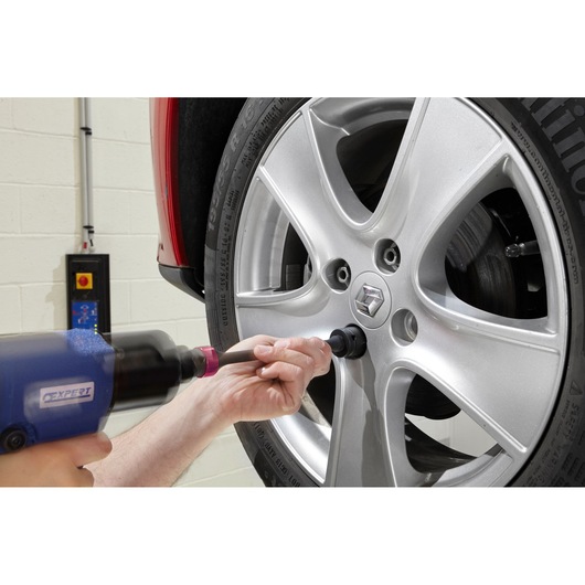 Facom E230110 socket in use on a car wheel, close-up side view, tool held by hand.
