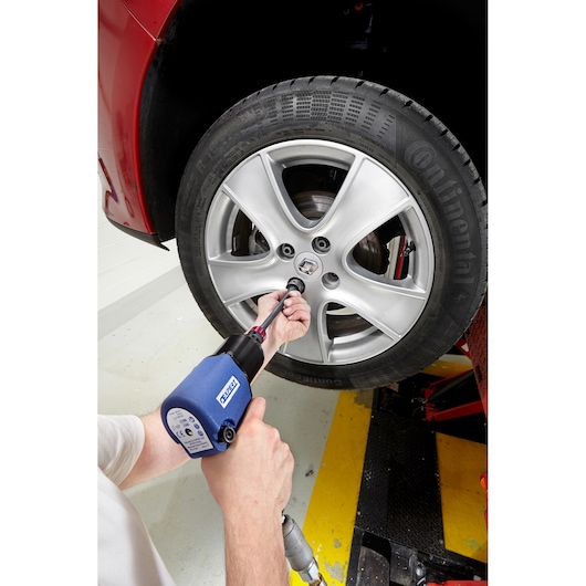 Facom E230110 impact wrench in use tightening lug nuts on car wheel, side angle photography.