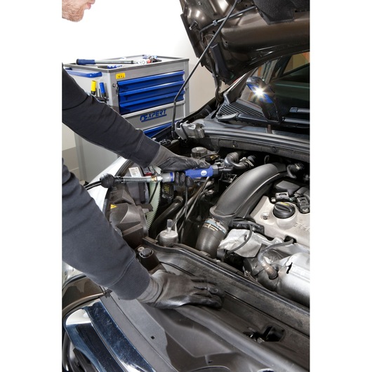 Facom E230201 mechanic using tool on car engine in workshop with blue tool cabinet in background.