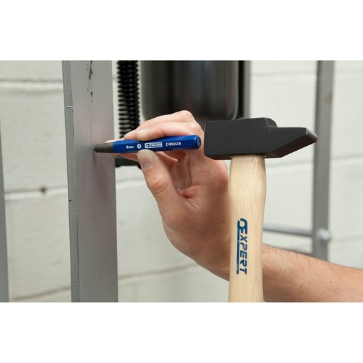 Facom E418227 blue steel punch held by hand with Expert hammer marking metal surface.