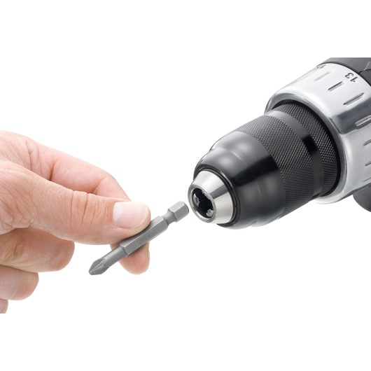 Facom ED_601T screwdriver bit being held near a drill chuck, white background, close-up.