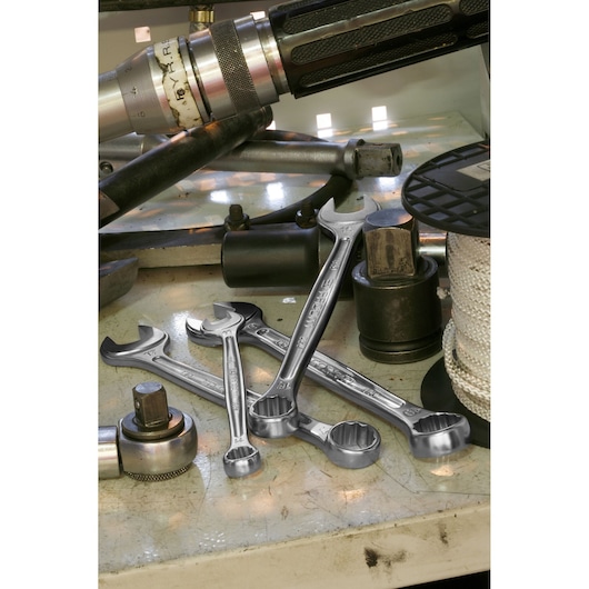 A close-up view of several Facom combination wrenches placed on a workbench among various mechanical tools and parts.