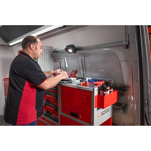 A person working at a red Facom tool cabinet inside a vehicle, with various tools and products organized on the cabinet's surface. The person's face is blurred for privacy.