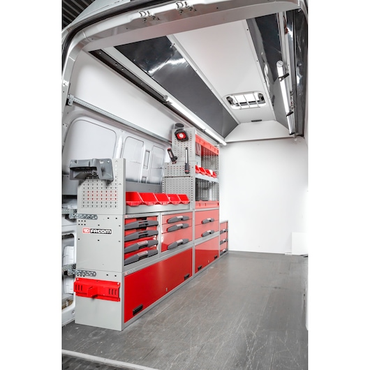 Interior view of a van equipped with red and grey Facom storage units, drawers and shelves, designed for organizing tools and equipment.