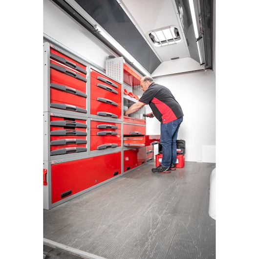 A person is organizing red Facom tool storage drawers inside a well-lit vehicle workspace. The drawers are mounted against the wall and labeled with the Facom logo.