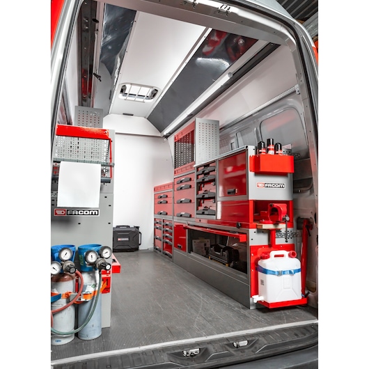 Interior view of a Facom-branded mobile workshop installed in a van, featuring organized red and grey storage cabinets, drawers, tool holders, gas cylinders, and a water container.