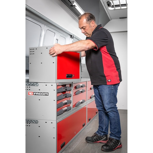 A person is organizing a red and grey storage unit with drawers and compartments inside a vehicle. The storage unit is branded with the Facom logo.