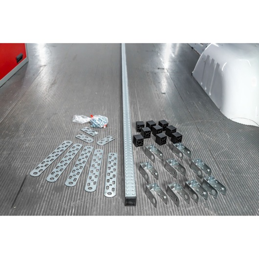 A set of metal brackets, perforated plates, black plastic connectors, screws in a plastic bag, and a long perforated metal rail laid out on a textured floor.