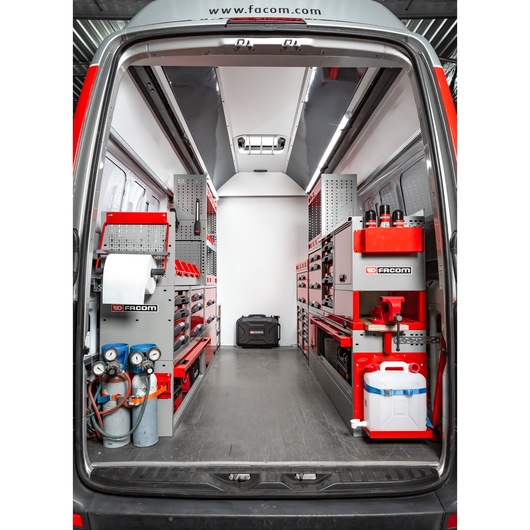 Interior view of a Facom-branded mobile workshop van, equipped with organized shelves, storage drawers, tool holders, gas cylinders, and cleaning supplies. The setup is designed for efficient tool storage and easy access during mobile service operations.