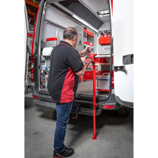 A person is operating a red Facom vise mounted on a workbench at the back of a van filled with organized tools and storage equipment.