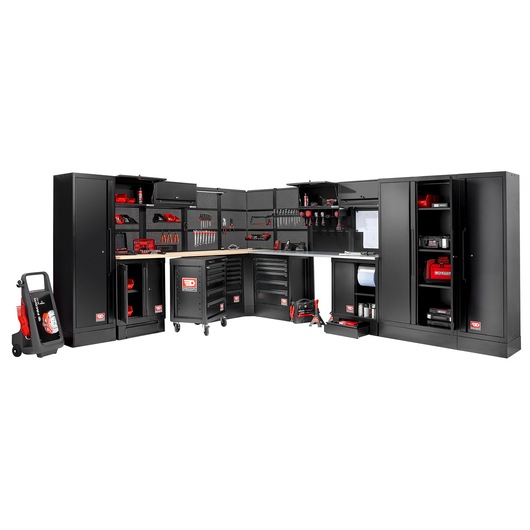 A large modular black tool storage system with multiple cabinets, drawers, and shelves, filled with various red and black tools and accessories. There are work surfaces and pegboards for tool organization. The setup is arranged in an L-shape, suitable for a workshop or garage.