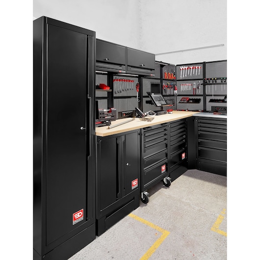 Black modular tool storage system by Facom, featuring cabinets, drawers, and pegboards with a variety of tools organized. The system has a wooden worktop and multiple compartments for tool storage in a workshop setting.