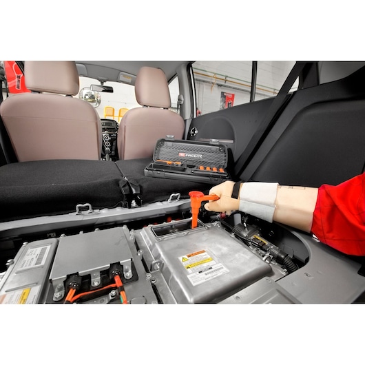 Facom J210AVSE insulated screwdriver set on car seat, technician using tool on electric vehicle battery.