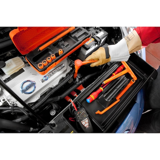 Facom J210AVSE insulated socket set in use on a Nissan electric car engine, hand with protective glove using a ratchet.