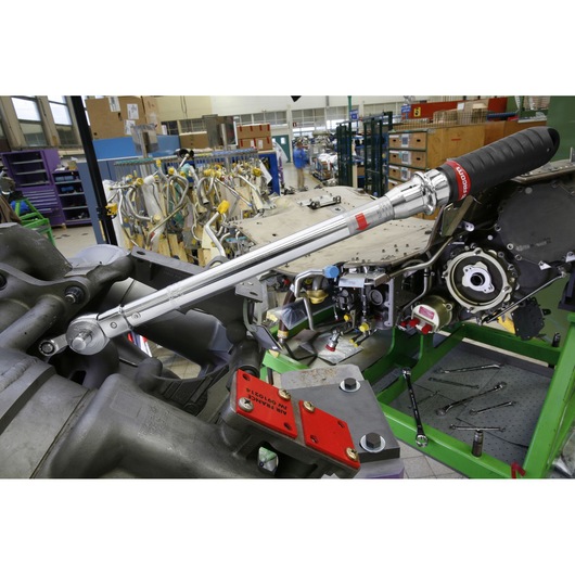 Facom J306A100 torque wrench with black grip in use on machinery in an industrial workshop, side angle.