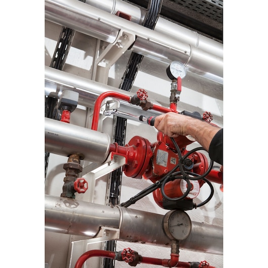 Facom JXL_171 hand tool used on industrial pipes with red valves and gauges, close-up photography.