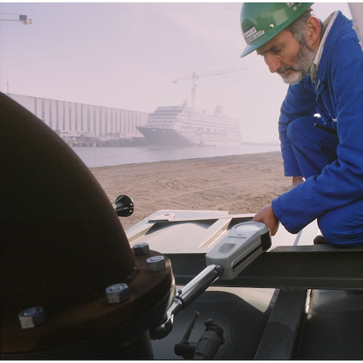 Facom K_201B torque wrench in use by worker in blue coveralls, industrial site with ship in background.