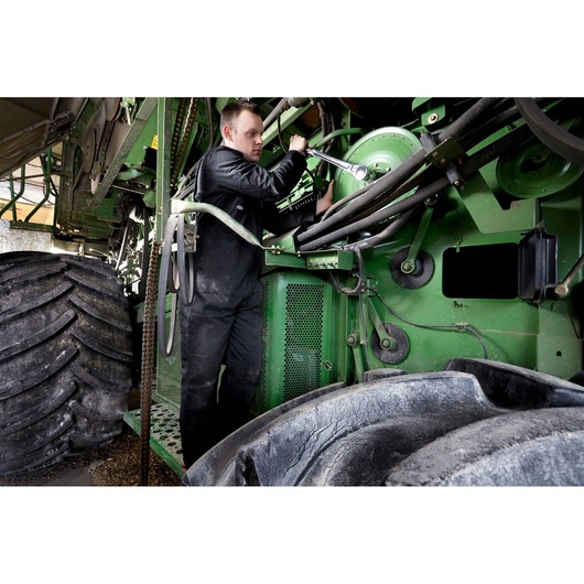 Facom KL_161 photography of mechanic using wrench on green agricultural machinery near large tires.