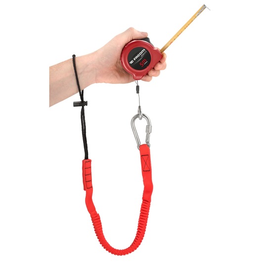 Facom LAN-WRT12 red safety lanyard with carabiner, securing a tape measure, shown worn on wrist, side angle.