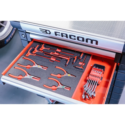 Open drawer of a Facom tool chest showing organized hand tools, including pliers, wrenches, and precision tools in foam inserts and holders.