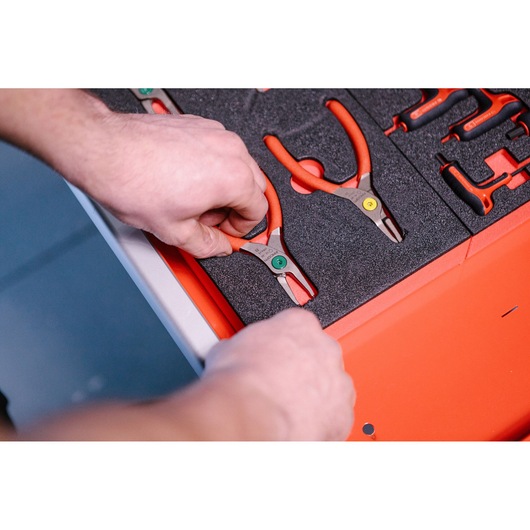 A person is placing or removing a pair of red-handled pliers from a foam tray in an organized tool drawer.