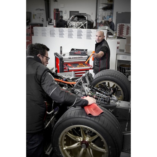 Facom MODM.VSEHYA photography of red tool chest with open drawers beside mechanics working on vehicle chassis.