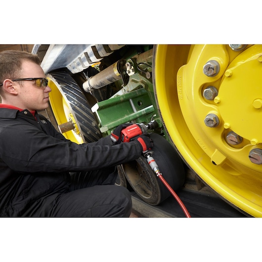 Facom NK.3000FPB impact wrench in use on yellow heavy machinery wheel, technician in black uniform.