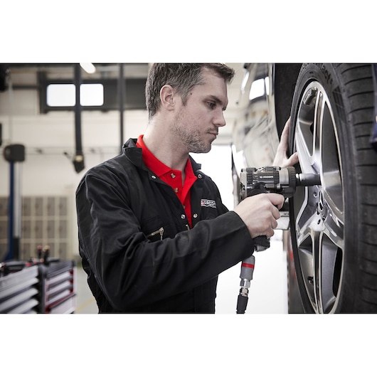 Facom NS2500G impact wrench in use tightening car wheel lug nuts in a workshop.
