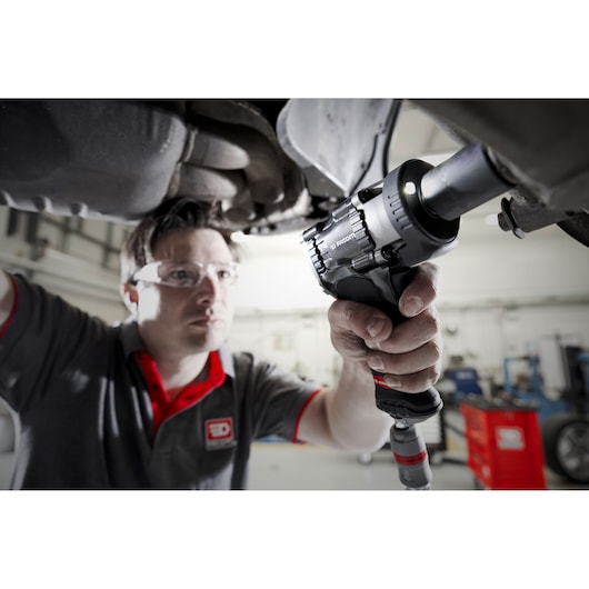 Photo of Facom NS2500G impact wrench used by mechanic under a vehicle in a workshop setting.