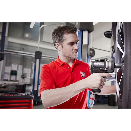 Photo of person in red polo using Facom NS.3500GPB impact wrench on car wheel in workshop.