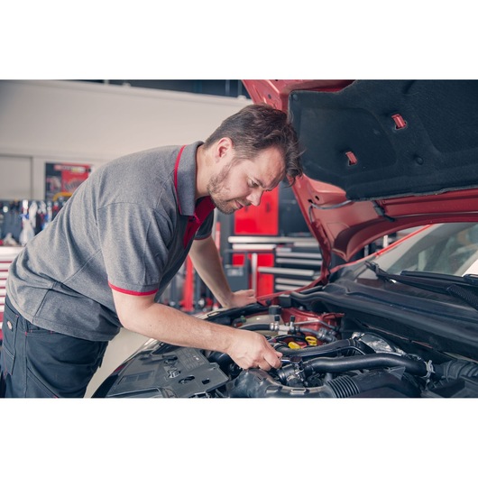 Facom R_181 mechanic working on car engine in workshop, wearing grey and red uniform. Photography.