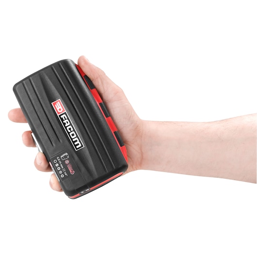 A hand holding a black and red Facom branded hard case, featuring a logo and some printed information on the front.