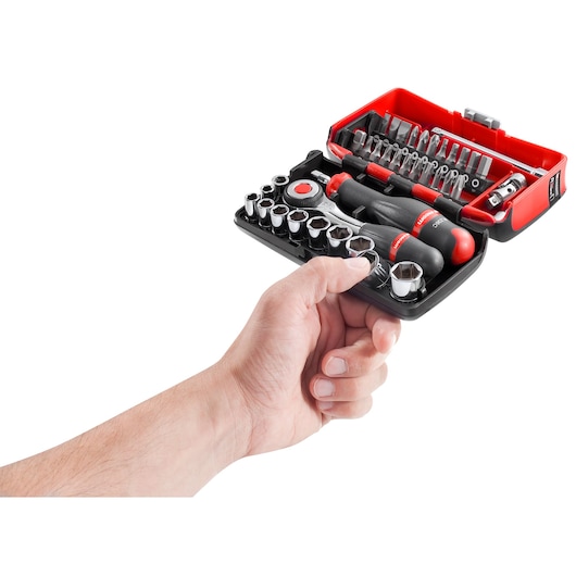 A hand holding a compact Facom tool kit, including a ratchet, screwdrivers, sockets, and various bits neatly organized in a red and black case.