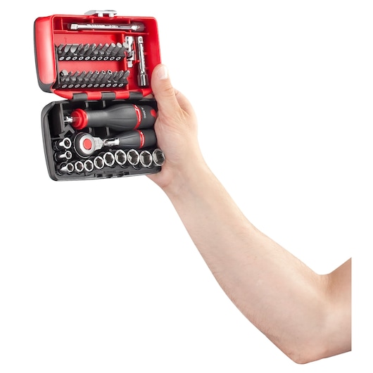 A hand holding an open Facom compact tool set containing a ratchet, screwdriver handle, sockets, and assorted bits, presented in a red and black plastic case.