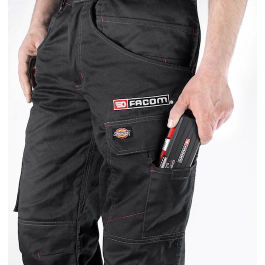Facom R1PICO compact tool set in hand, stored in black work trousers pocket, close-up, white background.