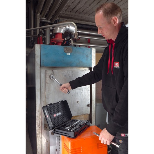 Facom S_151B socket set in black case on orange box, person using ratchet in industrial setting.