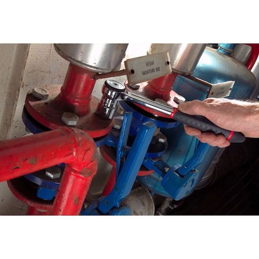 Facom S_161B ratchet wrench used on industrial valve pipes, close-up of hand holding tool.