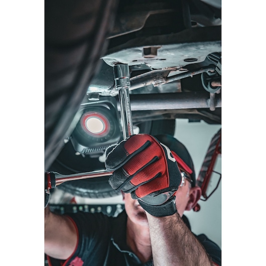 Facom S.17GRP ratchet wrench used under a vehicle, mechanic wearing red and black gloves, close-up photo.