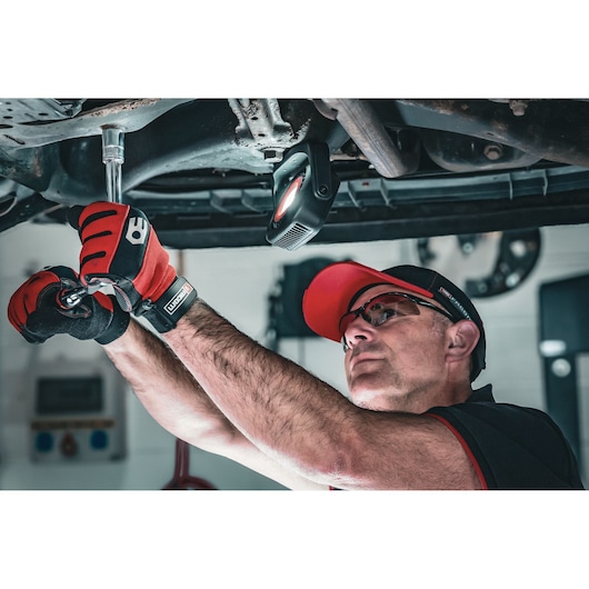 Facom S.17GRP ratchet wrench in use on automotive undercarriage, mechanic wearing red gloves and cap.