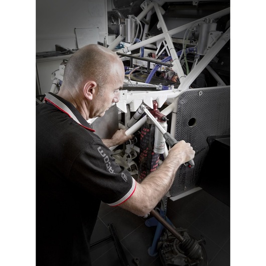 Photo of person using Facom S.209A100 torque wrench on white metal frame in workshop.