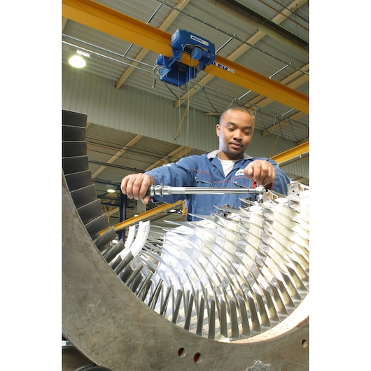 Facom S306A100 torque wrench used by technician on large industrial turbine, workshop setting, front view.