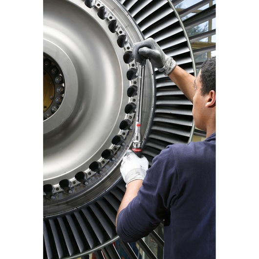 Photography of a person using a Facom S_306A350 torque wrench on a large industrial turbine.
