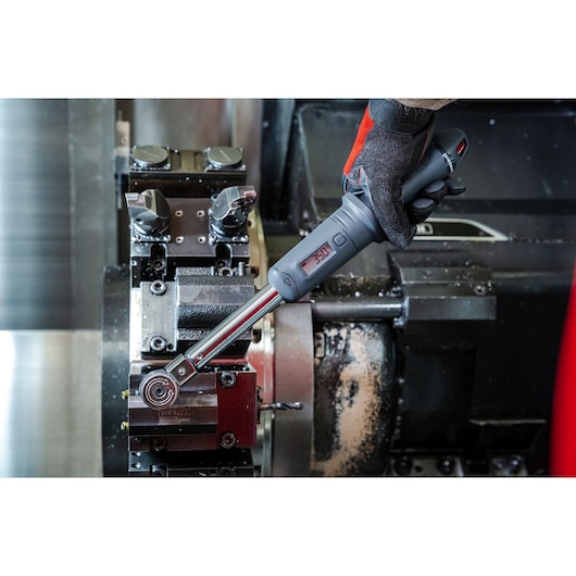 Facom S.307-100D digital torque wrench held by gloved hand adjusting machinery in workshop.