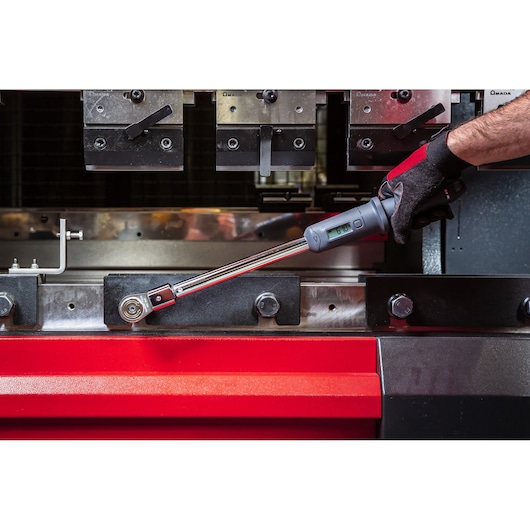 Photo of Facom S.307-100D digital torque wrench in use by a gloved hand, tightening a bolt on industrial machinery.
