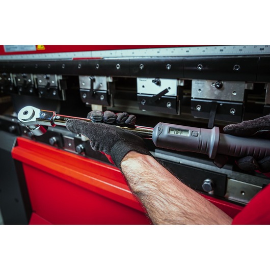 Facom S.307-100D digital torque wrench in gloves, used near industrial machinery.