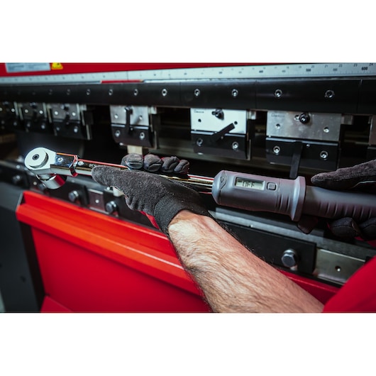 Facom S.307A200 digital torque wrench held by gloved hands in a workshop setting.