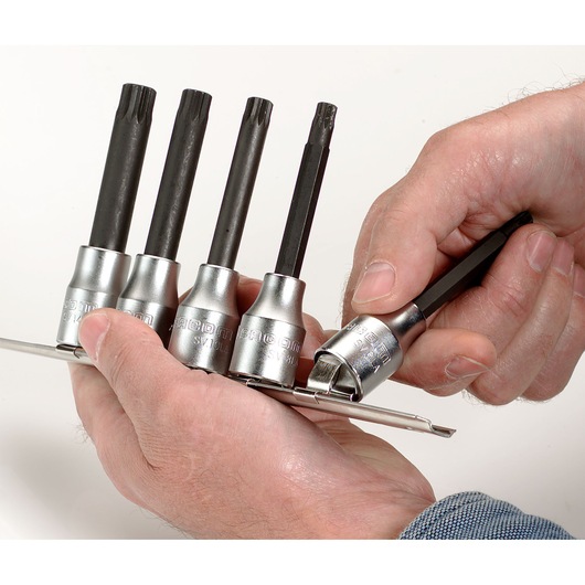 Facom SV_J5 socket bit set held in hand, four black bits with silver sockets on a metal rail, close-up.