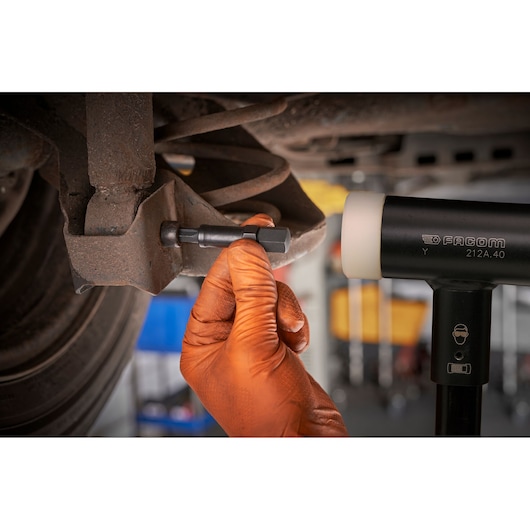 Photo of a gloved hand using a Facom mallet and tool on a car suspension, SXE_J7MGRPPB.