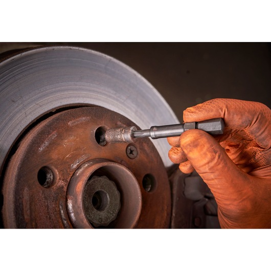 Facom tool SXE_J7MGRPPB used to remove a broken bolt from a rusty brake disc, close-up of gloved hand at work.