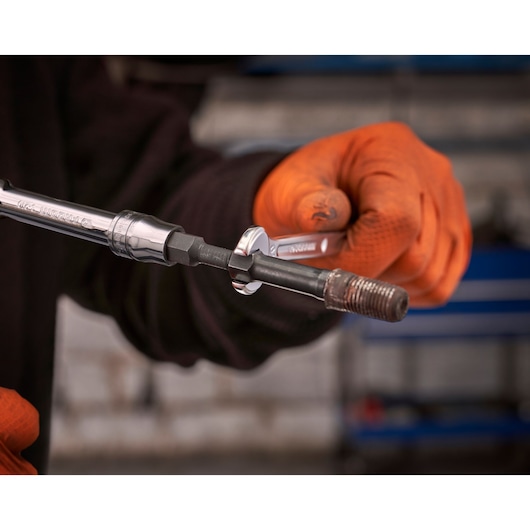 Facom wrench SXE_J7MGRPPB used on a hexagonal bolt, person wearing orange gloves, workshop background.